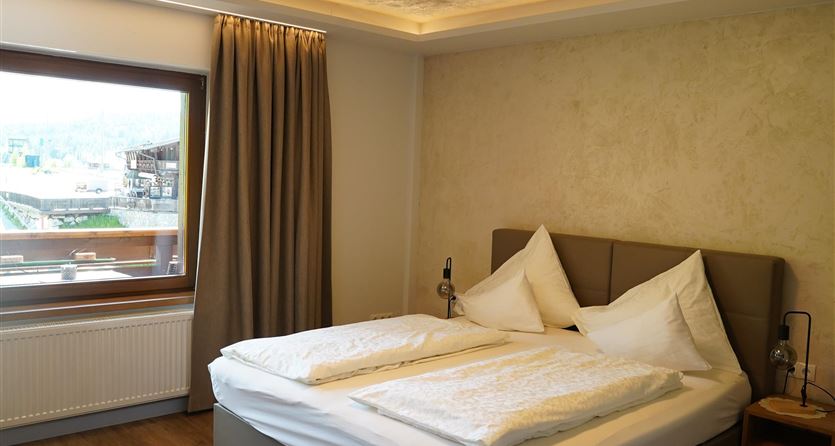 Een moderne slaapkamer met een groot bed en zacht licht. De muren zijn licht van kleur en de ramen bieden uitzicht naar buiten.