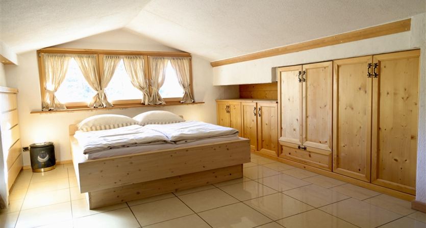 Een gezellige slaapkamer met een tweepersoonsbed en houten kasten. Grote ramen zorgen voor veel daglicht.