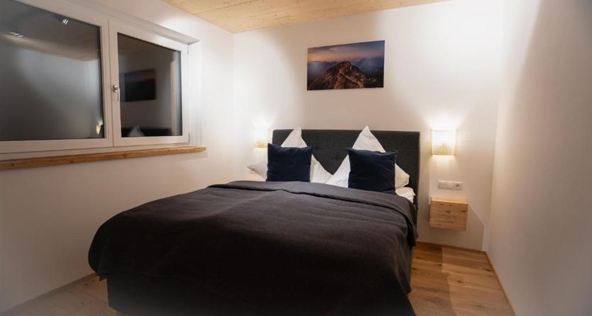 Ein gemütliches Schlafzimmer mit einem Doppelbett und modernen, minimalistischen Möbeln. Das Zimmer hat große Fenster, die für viel Tageslicht sorgen.