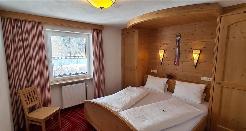 Een gezellige slaapkamer met een tweepersoonsbed en houten panelen. De ramen laten veel licht binnen en de ruimte is eenvoudig, maar uitnodigend ingericht.