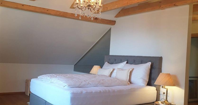 Una camera da letto accogliente con un grande letto e un elegante lampadario. I soffitti in legno e il design moderno creano un'atmosfera invitante.