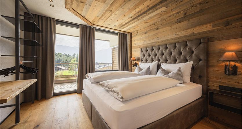 Una camera da letto moderna con pareti in legno e un grande letto. Le finestre offrono una vista sul paesaggio e garantiscono molta luce naturale.