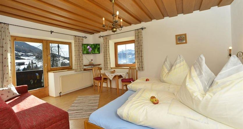 Een gezellige woonkamer met een tweepersoonsbed en een rode bank. Grote vensters bieden een mooi uitzicht op de bergen.