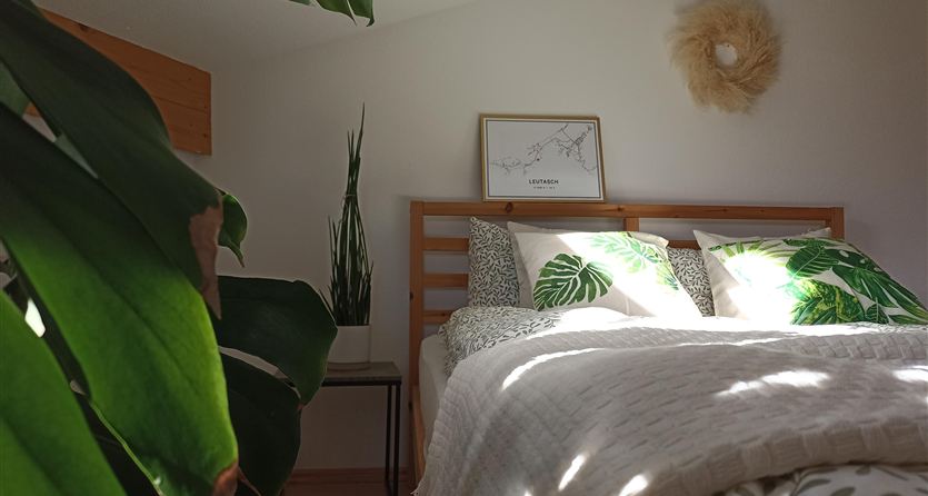 Una camera da letto accogliente con piante e biancheria da letto in design a foglie. La luce cade dolcemente sulla coperta del letto, creando un'atmosfera invitante.