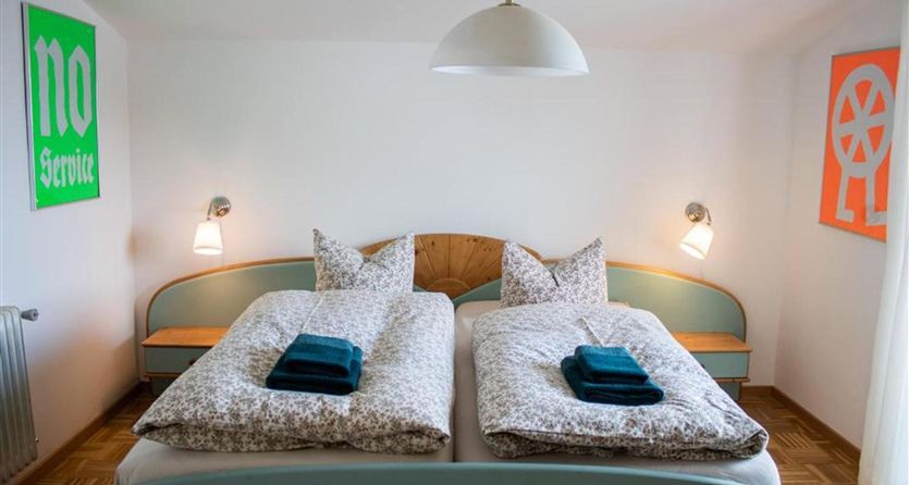 Una camera da letto luminosa con due letti singoli e opere d'arte moderne sulle pareti. La biancheria da letto è a fantasia e i cuscini sono piegati con cura.
