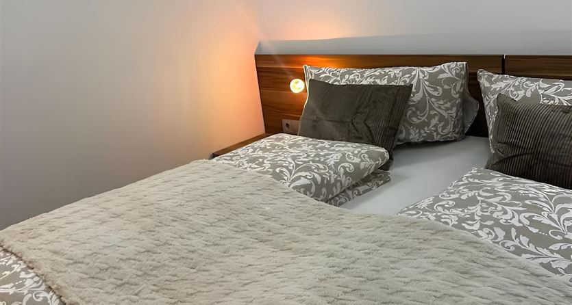Ein komfortables Doppelbett mit einer warmen Bettdecke und dekorativen Kissen. Die sanfte Beleuchtung schafft eine gemütliche Atmosphäre.