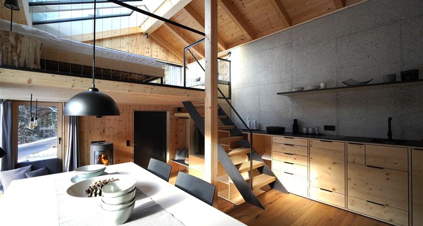 A modern, bright living room with wooden paneling and a staircase. The room has large windows and an inviting open atmosphere.