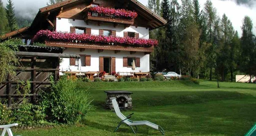 Een charmant huis met balkon en kleurrijke bloemen. Omringd door groene weiden en bomen onder een bewolkte hemel.