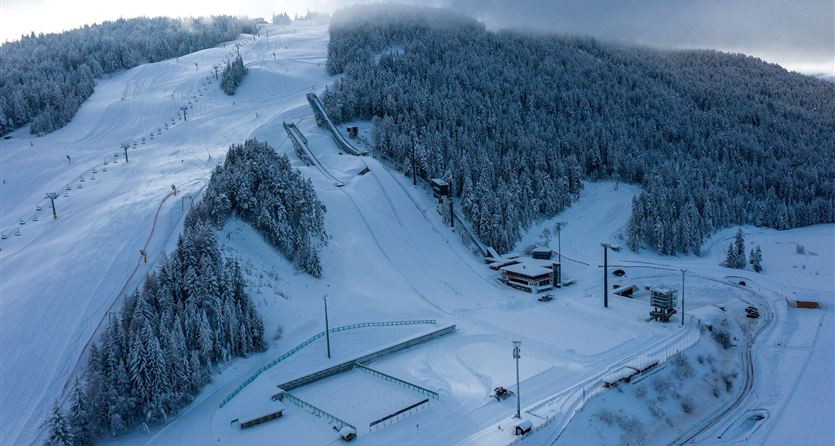 Un paesaggio innevato con piste e impianti di risalita. Gli alberi sono bianchi e le montagne sono disposte in forme dolci.