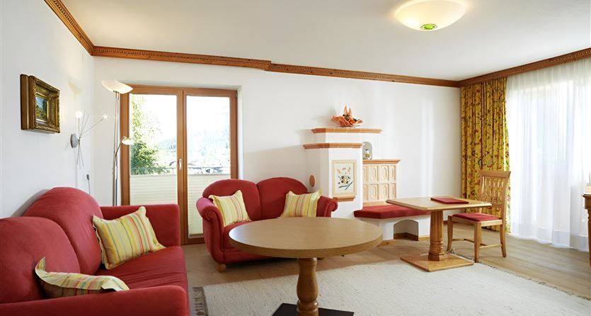 A bright living room with red sofas and a round table. Large windows allow plenty of light in and provide a view outside.