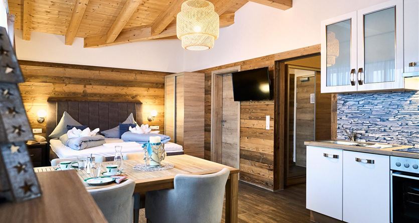 A modern, cozy room with wooden decor and a dining area. The open kitchen is equipped with modern appliances and creates an inviting atmosphere.
