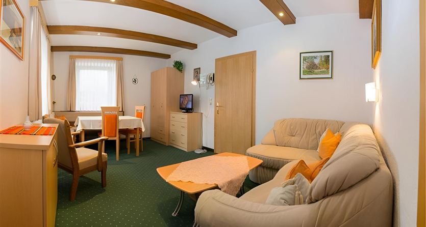 A cozy living room with comfortable sofas and a table. The room is bright and inviting, with a dining table in the corner.