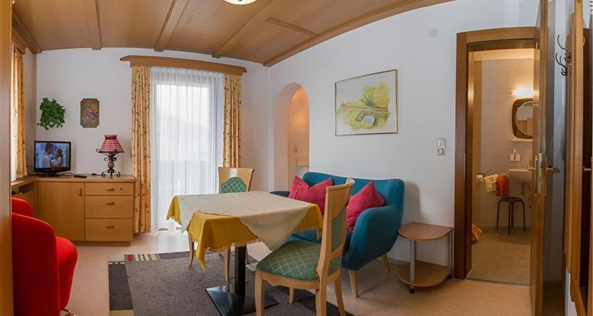 A cozy living area with a table and colorful armchairs. The walls are bright and cheerful, with a window that lets in plenty of light.