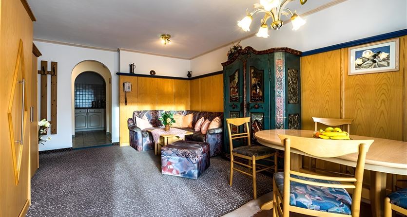 Ein gemütliches Wohnzimmer mit einer stilvollen Sitzecke und einem Esstisch. Die Wände sind mit Holzpaneelen verkleidet und ein traditioneller Schrank fügt Charme hinzu.