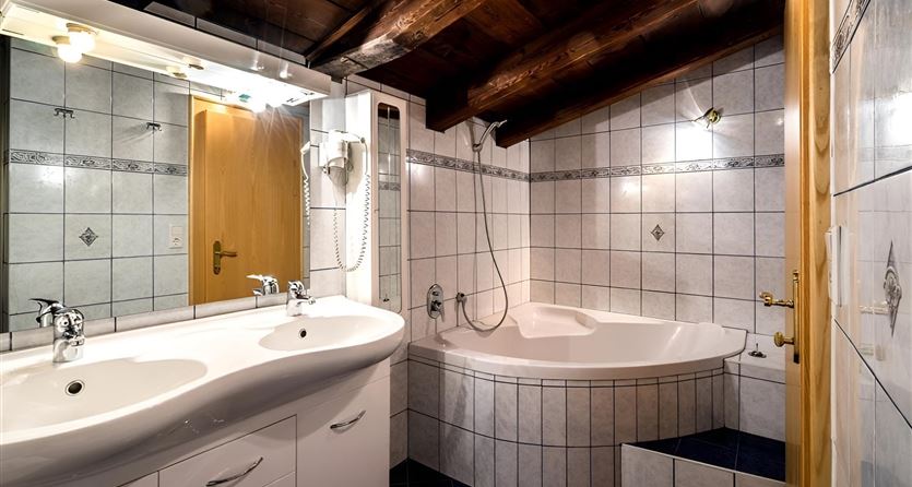 Ein modernes Badezimmer mit einer Badewanne und zwei Waschbecken. Die Wände sind mit Fliesen in neutralen Farben gestaltet und die Decke ist aus Holz.