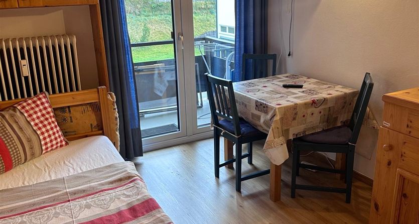 Ein gemütlicher Raum mit Holzverkleidung, einem Bett und einem Tisch mit Stühlen. Durch die Fenster hat man einen Blick auf die Umgebung.