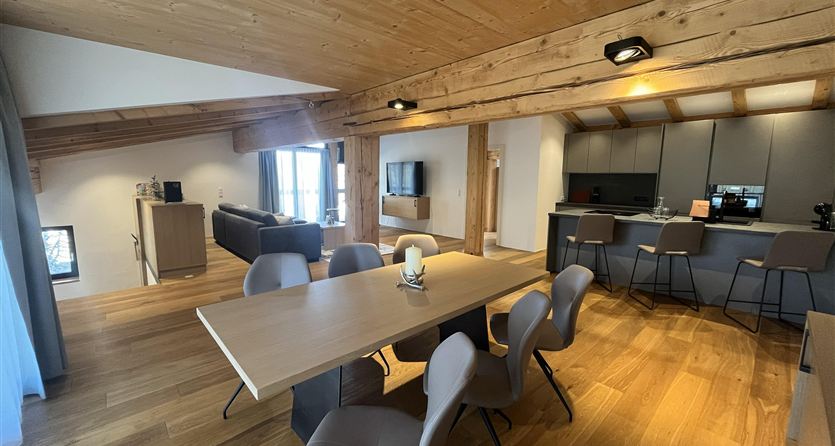 Ein modernes Wohnzimmer mit offenem Essbereich. Holzdecken und ein elegantes Design schaffen eine gemütliche Atmosphäre.