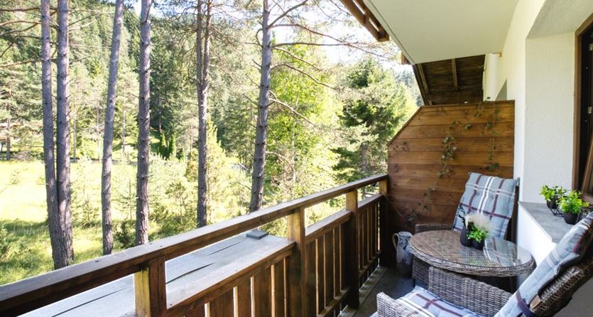 Ein gemütlicher Balkon mit Holzgeländer und bequemen Sitzgruppen. Im Hintergrund sind grüne Bäume und eine ruhige Landschaft zu sehen.