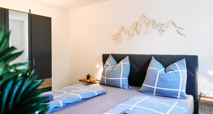 Una camera da letto accogliente con due letti e cuscini moderni. Sulla parete ci sono silhouette di montagne decorative e c'è un'illuminazione elegante.