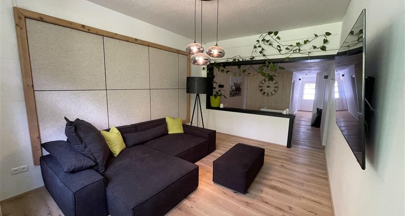 Een moderne woonkamer met een elegante zwarte bank en een salontafel. De lichte houten vloeren en planten creëren een aangename sfeer.