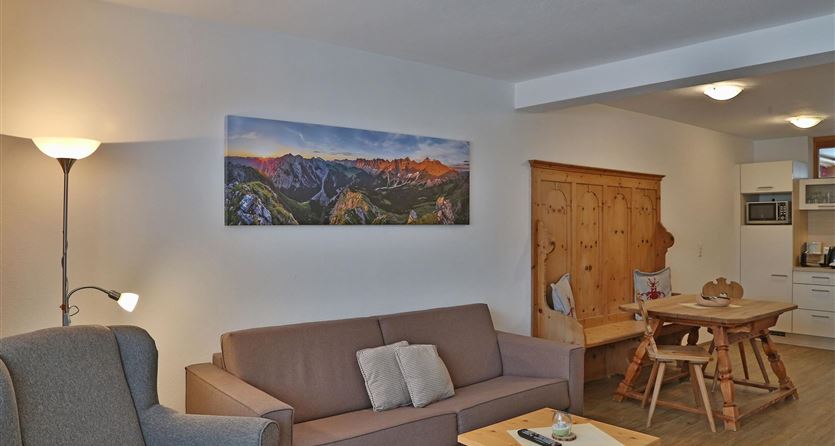 Un salotto accogliente con un divano grigio e un grande armadio di legno. Sulla parete è appesa un'immagine panoramica di montagne.