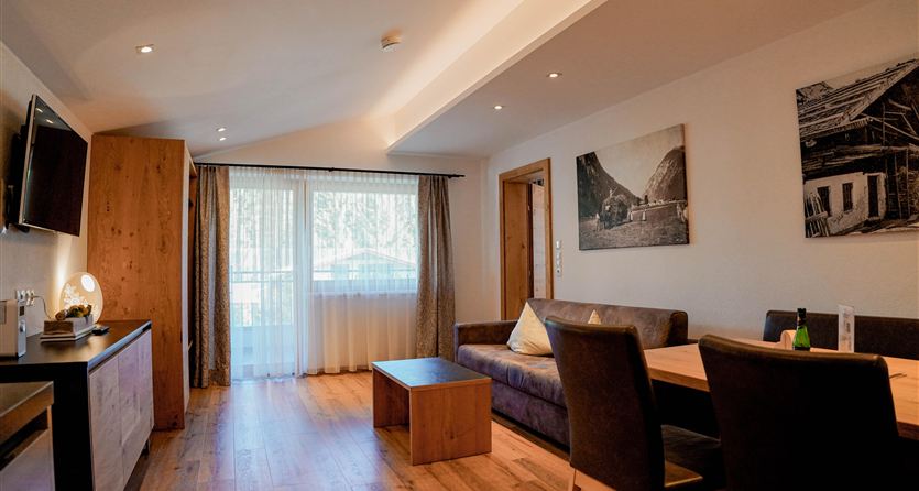 Ein moderner, geräumiger Wohnbereich mit Holzfußboden und großen Fenstern. Der Raum hat eine Couch, einen Essecke und helle Wände.