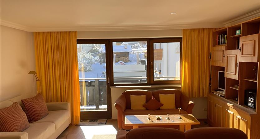 Ein gemütliches Wohnzimmer mit einem hellen Sofa und einem Couchtisch. Große Fenster lassen viel Tageslicht herein und bieten einen Blick nach draußen.