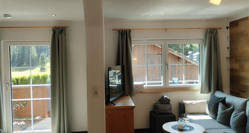 Een lichte woonkamer met een comfortabele bank en grote ramen. Het uitzicht toont een groene buitenruimte en een rustige omgeving.