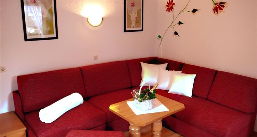 Een gezellige woonkamer met een rode bank en een houten tafel. Aan de muren hangen schilderijen en een plant is decoratief geplaatst.