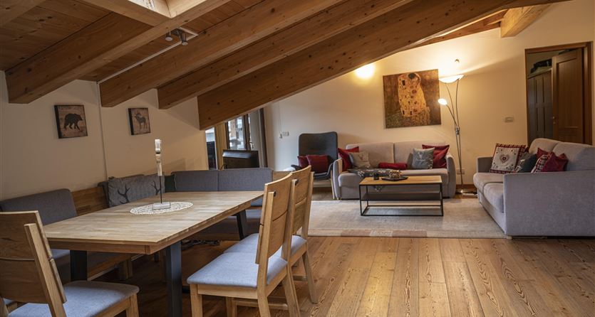 Ein gemütliches Wohnzimmer mit Holzbalken und einem Esstisch aus Holz. Die Einrichtung ist modern mit einem hellen Teppich und einer angenehmen Beleuchtung.