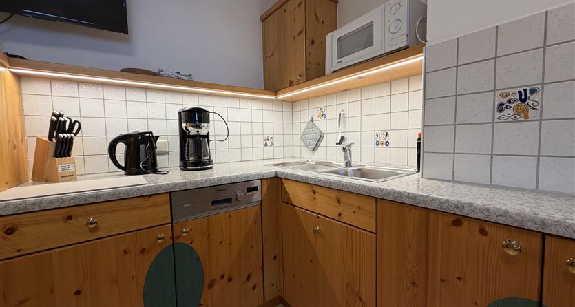 Een moderne keuken met houten kasten en heldere verlichting. Op het aanrecht staan een koffiezetapparaat en een waterkoker.