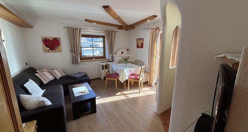 A cozy living room with a black sofa and a dining area. Large windows provide plenty of daylight and a pleasant atmosphere.
