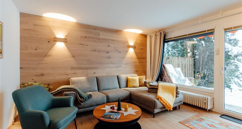 Un soggiorno moderno con un comodo divano e un tavolino rotondo. Grandi finestre con vista sulla natura e illuminazione calda creano un'atmosfera accogliente.