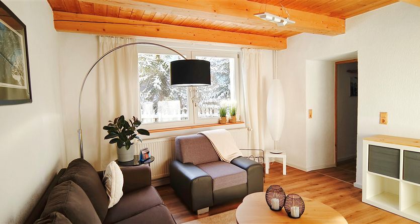 Un soggiorno accogliente con una grande finestra e luce naturale. L'arredamento è composto da un divano grigio, una sedia e un tavolo rotondo.