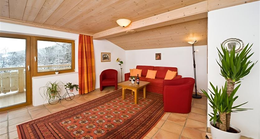Un soggiorno accogliente con mobili rossi e una grande zona finestrata. La stanza ha un soffitto in legno e un bel tappeto.