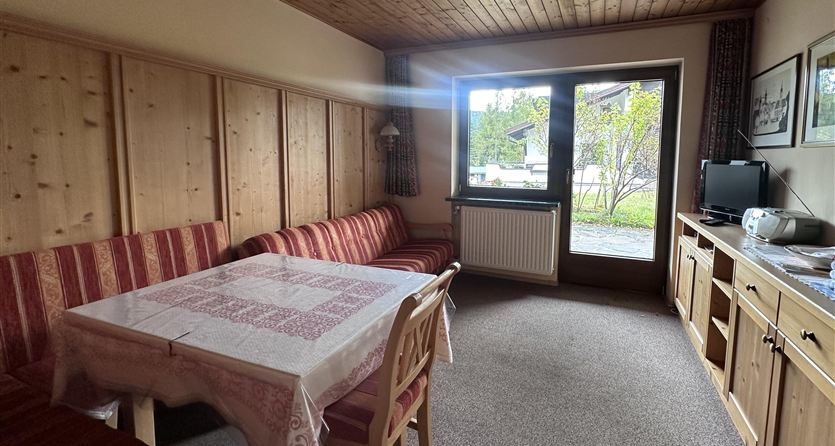 Ein gemütliches Wohnzimmer mit Holzdecke und einer Sitzecke. Am Fenster ist ein Tisch mit Blick auf den Garten.