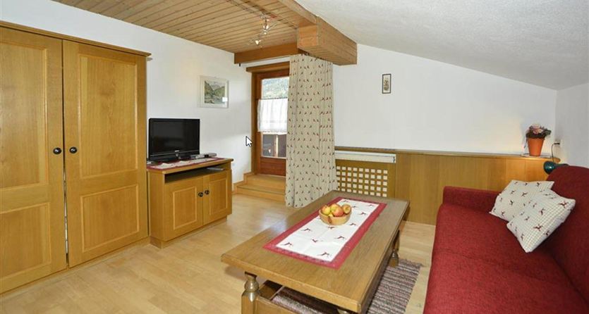 Een gezellig woonkamer met een rode bank en een houten tafel. Aan de muur staat een televisie en een grote houten kast.