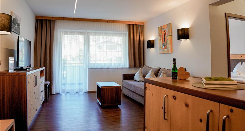 Ein modernes Wohnzimmer mit einem Sofa und einem Tisch. Große Fenster lassen viel Licht herein und der Raum wirkt einladend.