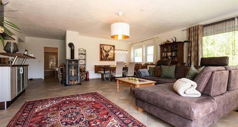 A modern living room with a comfortable sofa and a cozy rug. The space is bright and welcoming, with a table and chairs in the background.