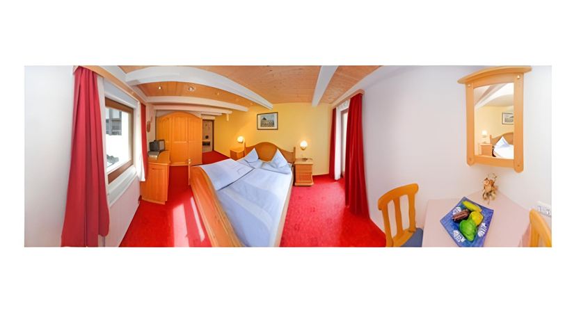 Ein helles Zimmer mit zwei Betten, roten Teppichen und Holzdekor. Große Fenster und ein Spiegel sorgen für eine einladende Atmosphäre.