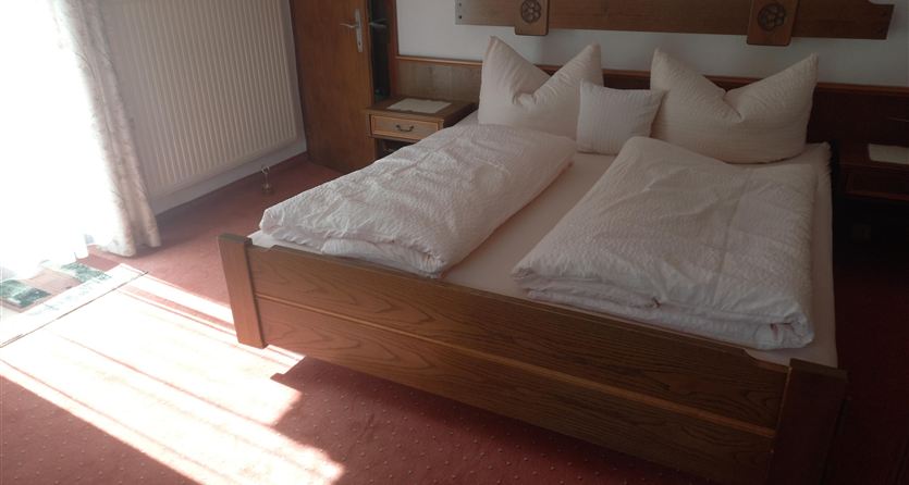 Una camera da letto accogliente con un letto matrimoniale e grandi cuscini. La luce del sole filtra attraverso le finestre creando un'atmosfera luminosa e accogliente.