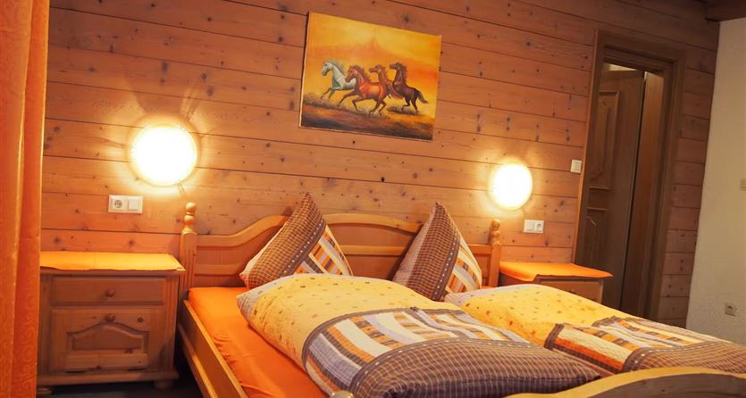 Een gezellig slaapkamer met houten wandbekleding en een tweepersoonsbed. Aan de muur hangt een schilderij van paarden, en de kamer heeft warm licht door twee lampen.
