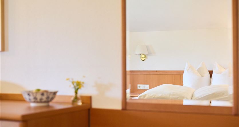Ein gemütliches Zimmer mit einem großen Spiegel. Im Hintergrund sind ein Bett und ein Nachttisch zu sehen.