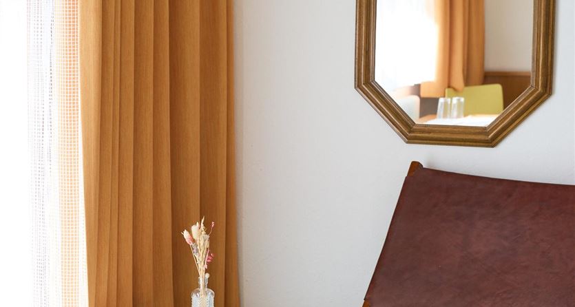Ein stilvolles Wohnzimmer mit einer Holzliege und einem runden Tisch. Die Wände sind mit goldfarbenen Vorhängen und einem Spiegel dekoriert.