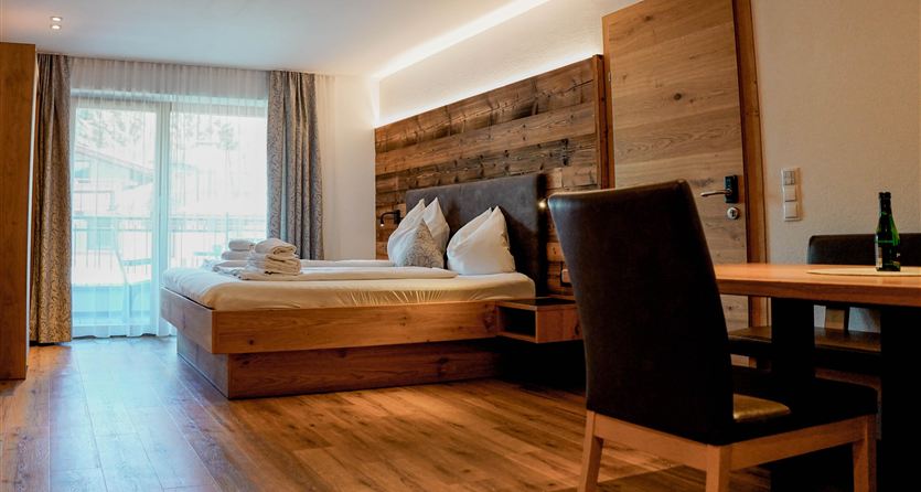 Ein modernes Hotelzimmer mit zwei Betten und Holzmöbeln. Es gibt einen Tisch, einen Stuhl und große Fenster, die viel Licht hereinlassen.