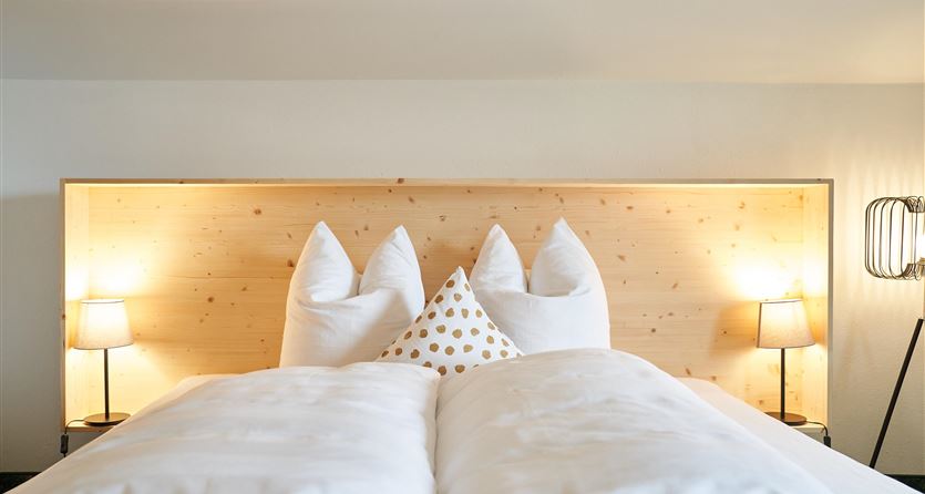 Ein gemütliches Schlafzimmer mit einem großen Bett und weißen Bettdecken. Zwei Nachttische mit Lampen ergänzen die helle, einladende Atmosphäre.