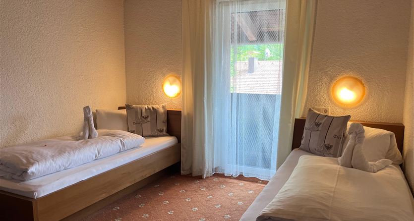 Een gezellige slaapkamer met twee eenpersoonsbedden en zachte verlichting. Het raam laat veel daglicht binnen en biedt uitzicht naar buiten.