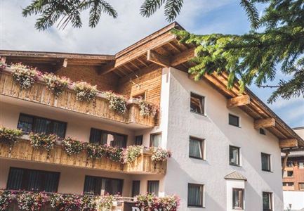 A charming café-restaurant with flower balconies in the Alps. The entrance area is inviting, and guests are standing in front of it.