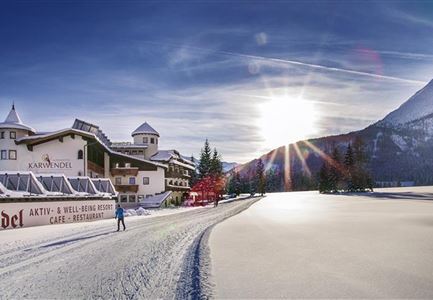 Ein schneebedecktes Landschaftsbild mit einem Ferienhaus in den Bergen. Die Sonne geht hinter dem Berg auf und erhellt die Szene.