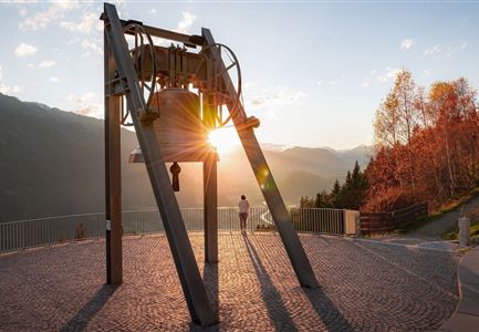 Friedensglocke im Herbst - Frau steht am Geländer und blickt ins Inntal beim Sonnenuntergang- Sonnenstern an der Glocke.jpg